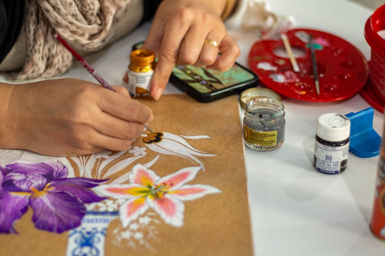 Artist painting vibrant flowers on paper using gouache paints in an indoor setting.
